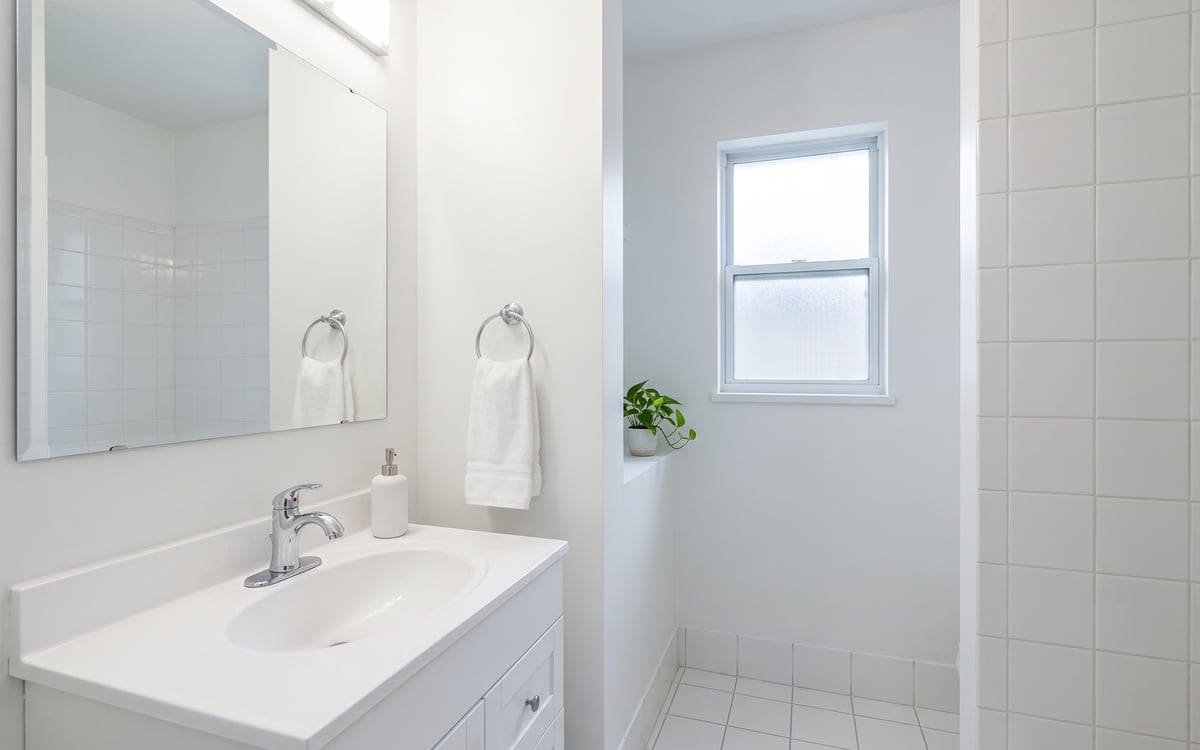 A small guest bath after a one time cleaning service, its white vanity dry around the chrome faucet and a fresh hand towel hanging on the ring.