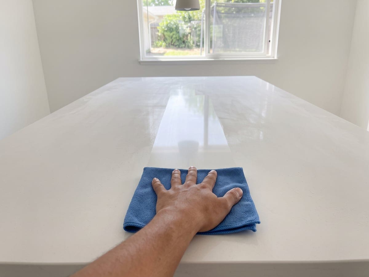 Post construction cleaning in a San Diego kitchen, a bare hand on a blue cloth leaving one glossy lane through the fine dust on a white island.